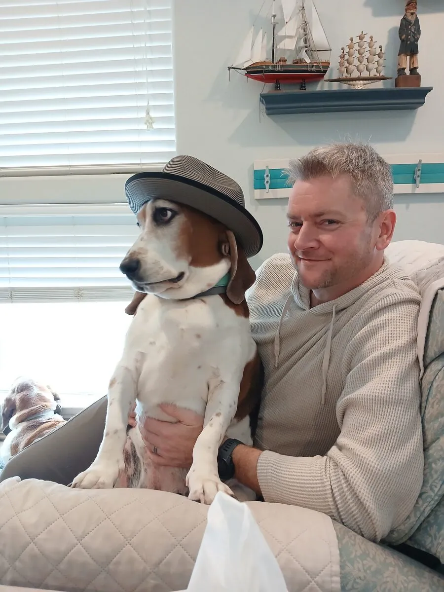 One of Jared's basset hounds wearing his fedora, sitting beside him on the couch