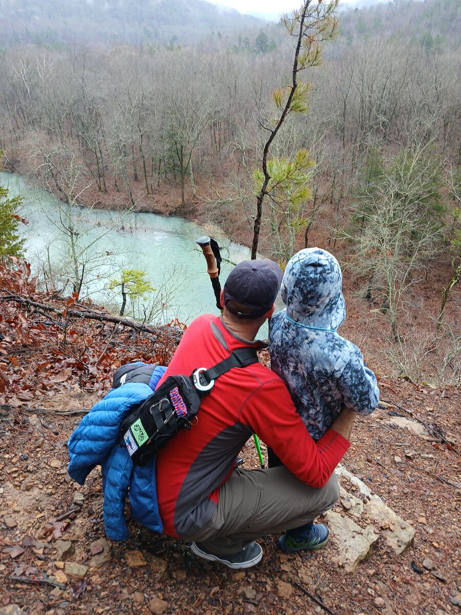 Jared and his son Levi crouched on a bluff overlooking a river on a misty hike