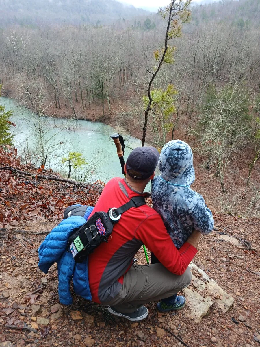 Jared and his son Levi crouched on a bluff overlooking a river on a misty hike