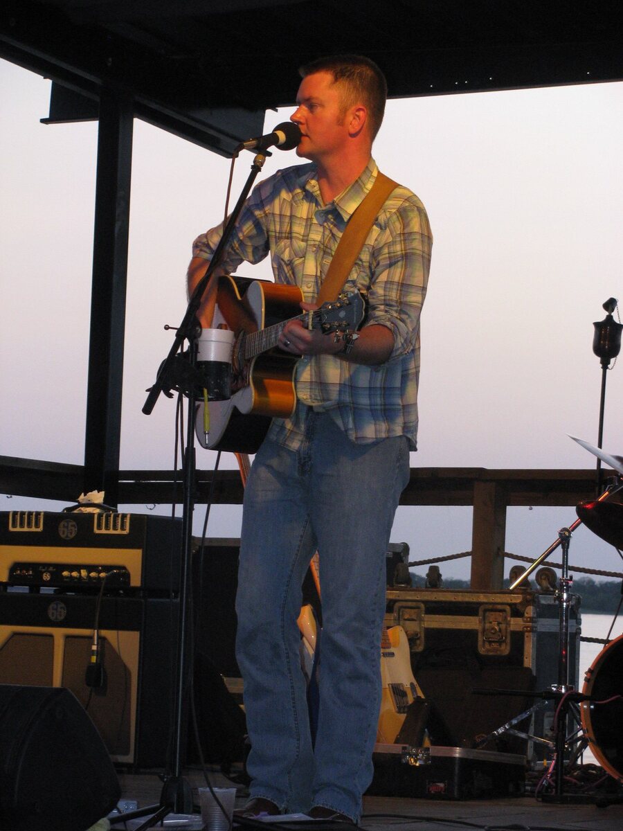 Jared performing on stage with an acoustic guitar at sunset during his professional music days