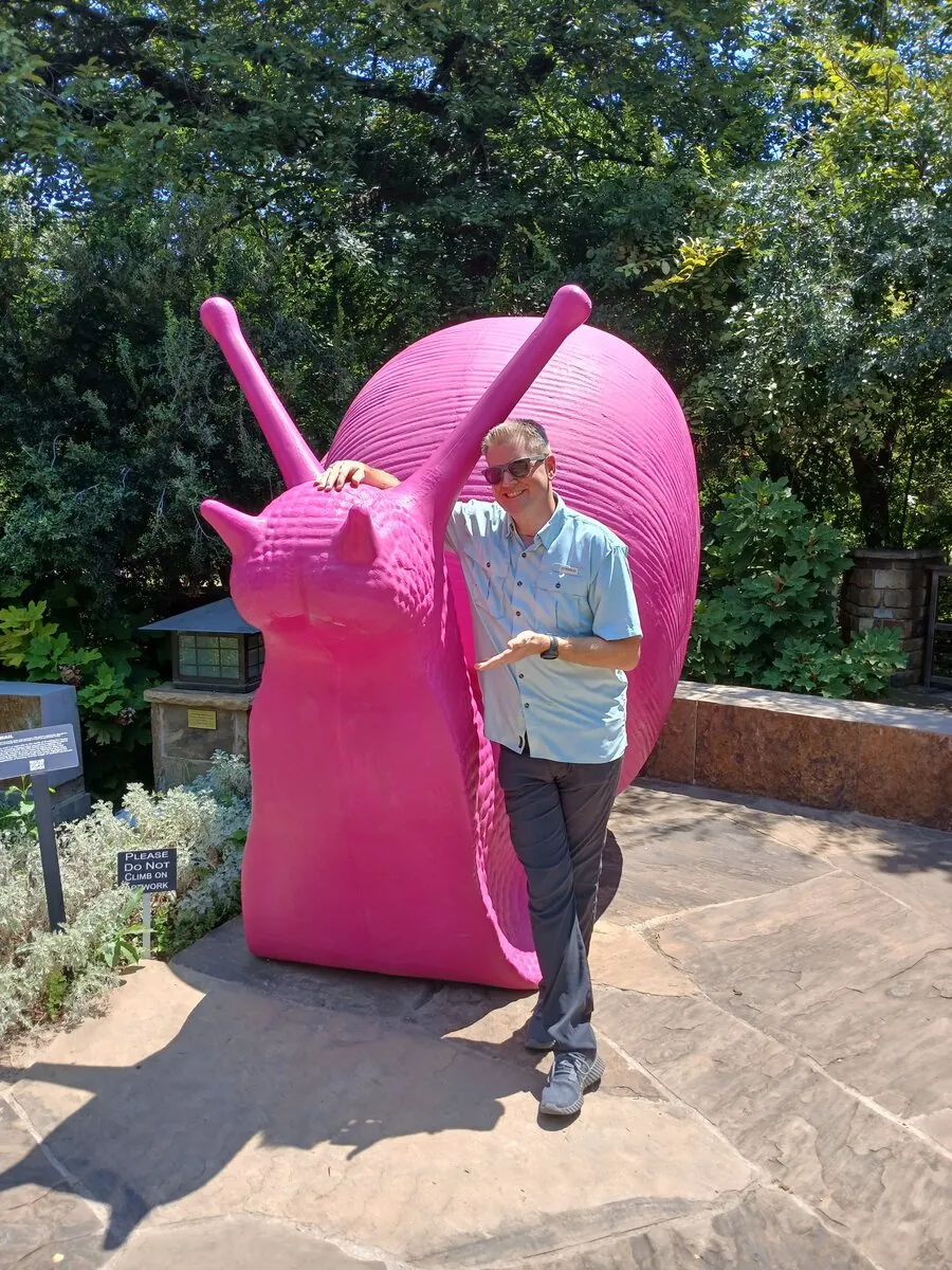 Jared posing proudly next to a giant pink snail sculpture