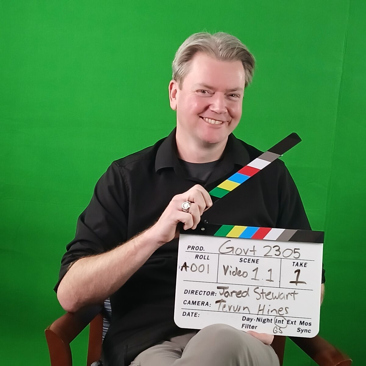 Jared on set with a production clapperboard, filming course videos for GOVT 2305