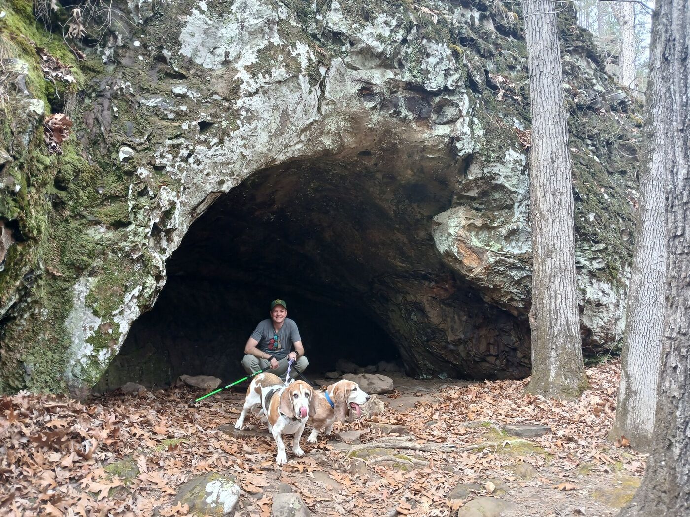 Jared on a hiking trail with two basset hounds in front of a cave