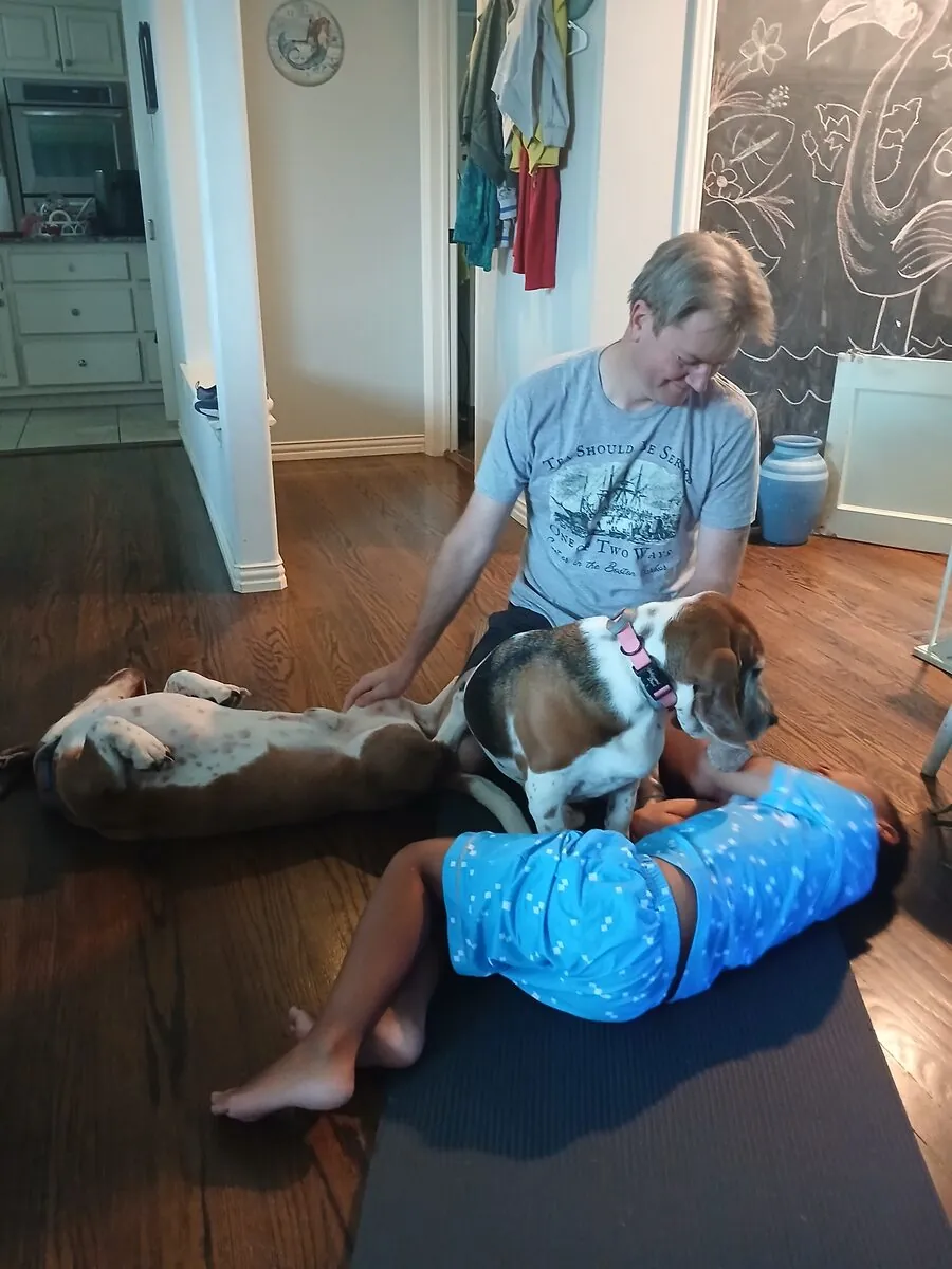 Jared and Levi doing floor stretches while two bassets supervise and sprawl